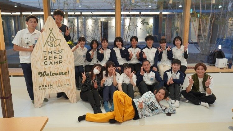 『THE SEED CAMP Welcome!』と書かれた木製の看板の前に、20人ほどが集まっている集合写真