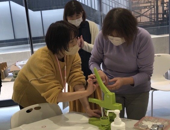 緑色の缶バッジ製作機を使って、3人が缶バッジを作っている
